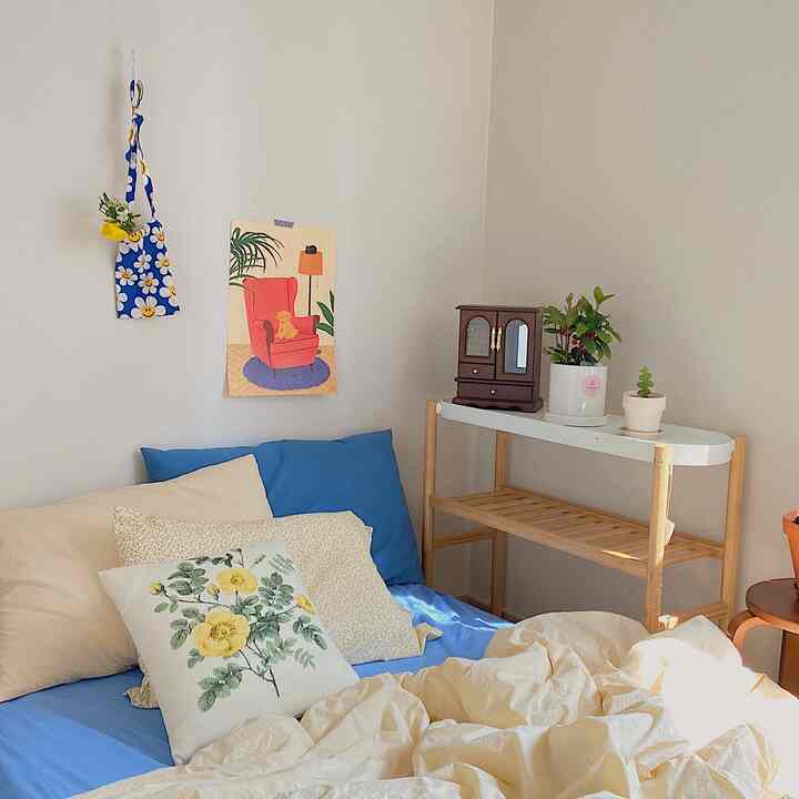 Beige and blue toned bedroom featuring bed with pillows and blankets, next to a shelf with plants creating cozy atmosphere