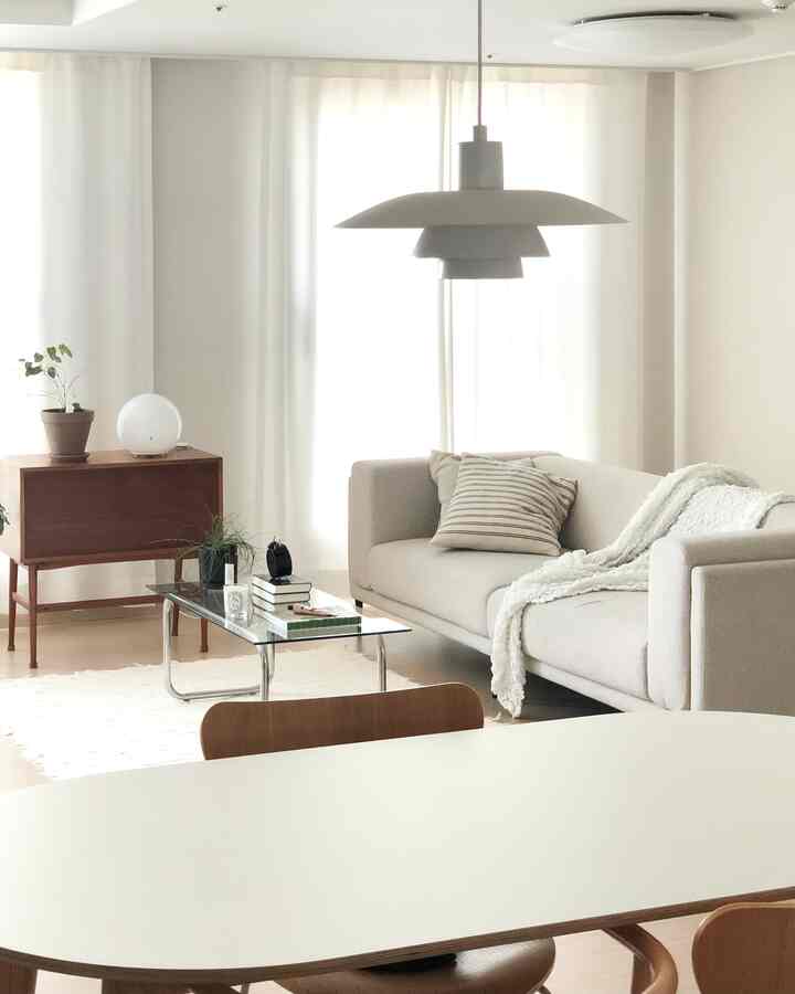 Bright white and beige toned living and dining room featuring beige fabric sofa, glass table, wooden furniture in a natural modern minimalistic style