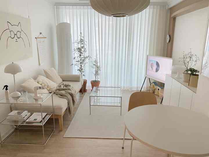 白とベージュの色合いのリビング、丸テーブルとソファ、透明なサイドテーブルが配置された自然なモダンなインテリア