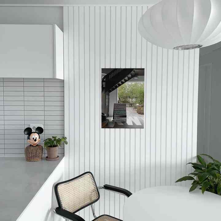 White-toned kitchen and dining area featuring rattan chair and poster creating a modern and clean atmosphere