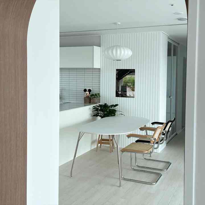Clean white-tone kitchen and oblique dining table with rattan armchairs create a cozy, modern dining space