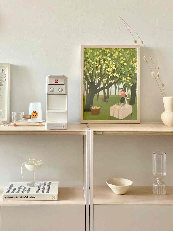 White-toned wall featuring white wood cabinets with illy coffee machine, picture frames, and ceramic vase creating a clean and airy space