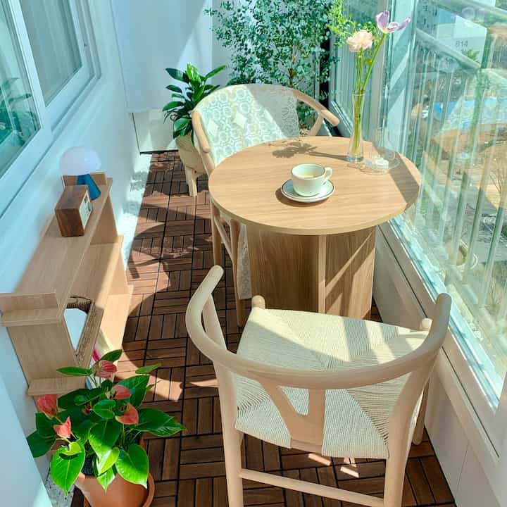 Bright wood tone and white veranda cafe featuring round table, chairs, and plants in a cozy home cafe setting