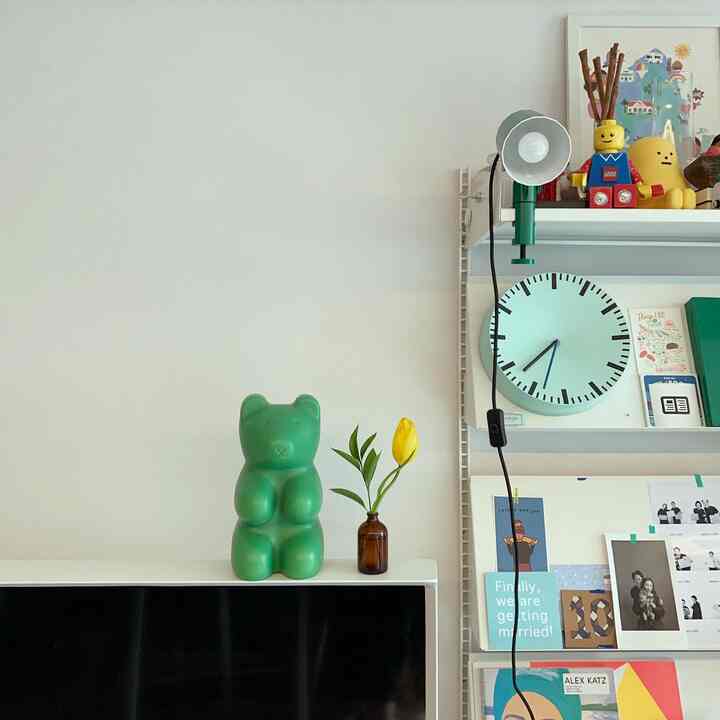 Clean living room with white walls and shelves, featuring a green bear lamp and yellow tulip vase