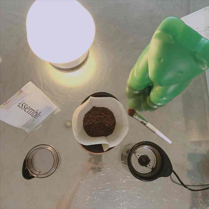 シルバーのステンレスキッチンアイランドの天板に、ハンドドリップコーヒーセット、明るいランプ、緑色のクマのオブジェが置かれた印象的なキッチンスペース