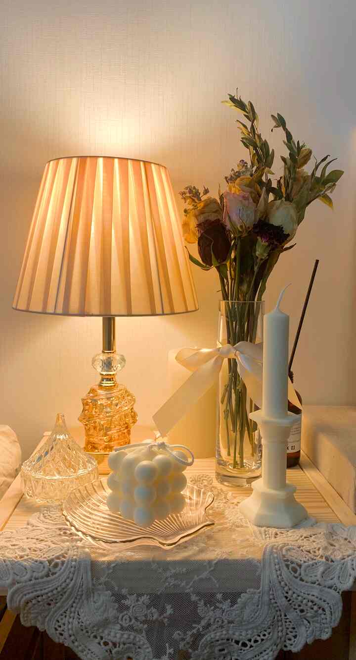 Cozy table setting in warm beige and white tones featuring candles, a table lamp, and dried flowers for decorative ambiance