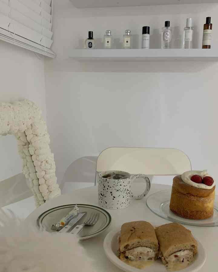 白を基調としたリビング、円形テーブルと透明な椅子が配置され、デザートとコーヒーがある清潔感のある空間