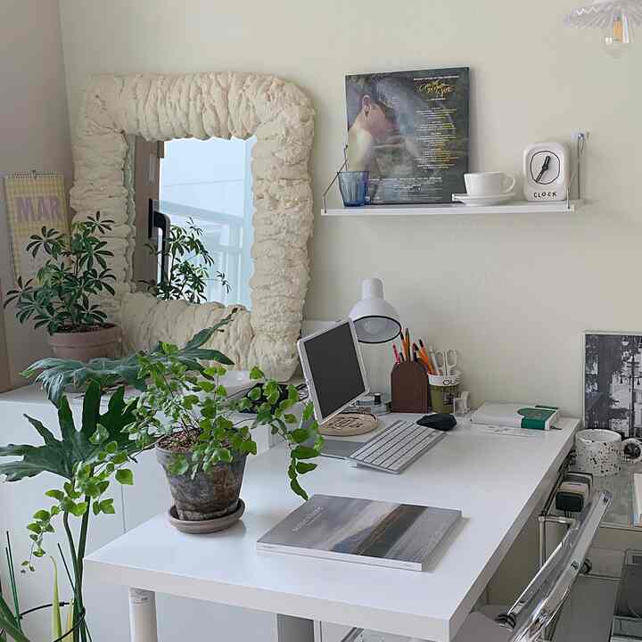 White-toned home office space featuring a simple desk, storage cabinet, and plants adding natural touches