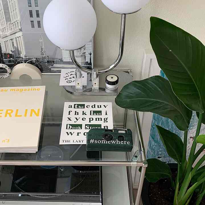 Modern interior with white walls and transparent glass table, featuring posters and green plants harmoniously arranged