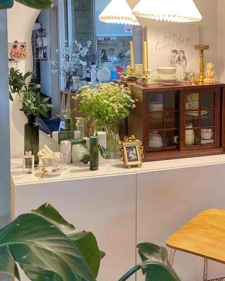 White and wood tone living room corner featuring cabinet with vases, plants, and a large mirror creating a cozy atmosphere