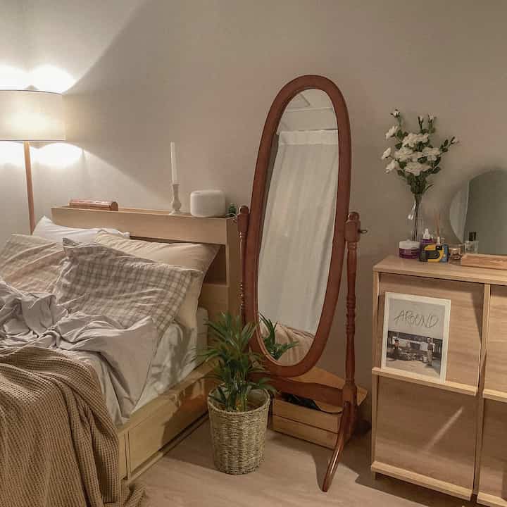 ベージュと木目調が調和する温かみのある寝室、木製の全身鏡とドレッサーが配置されたナチュラルモダンなインテリア