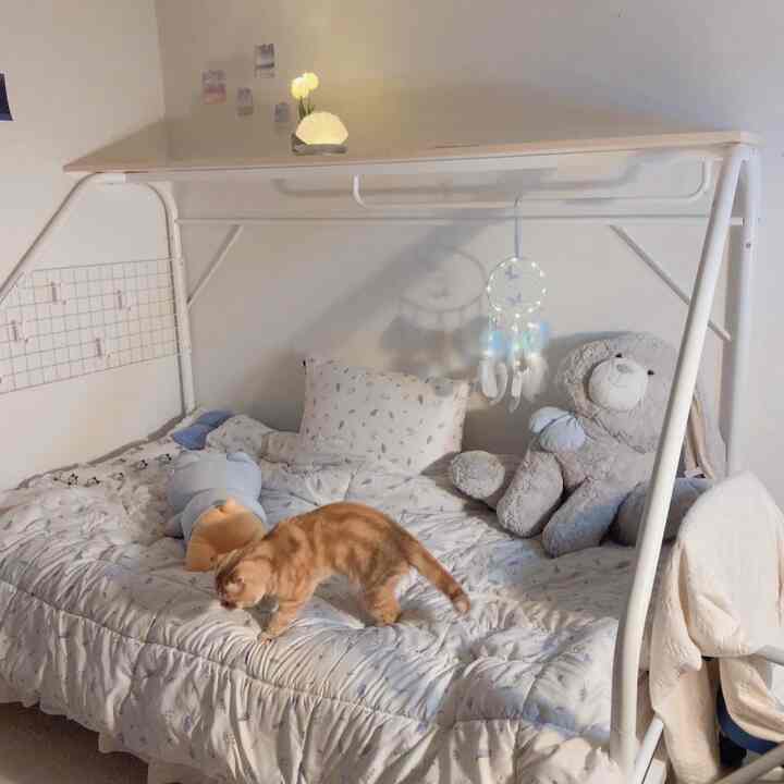 白と淡いグレーのトーンの寝室、キャットタワーとして使われる棚とベッドの上の猫が配置された雰囲気のあるインテリア