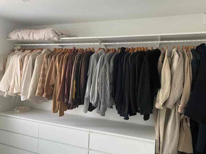 白を基調としたウォークインクローゼット、木製ハンガーにかけられたブラウンや黒の衣服が整然と並ぶ雰囲気のあるインテリア