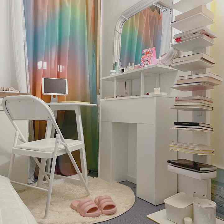 明るいホワイトトーンの寝室、カラフルなカーテンと円形テーブル、折りたたみ椅子、化粧台が配置された印象的な空間