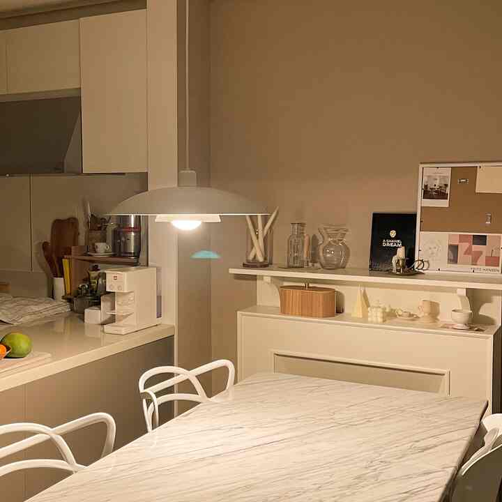 White and beige toned kitchen space featuring a marble dining table centered under pendant lighting, minimal and cozy interior