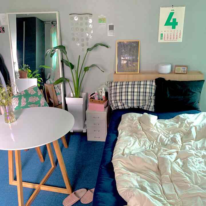 ブルーとホワイトの色調の寝室、ネイビーベッドと白い掛け布団カバー、丸テーブルと大きな観葉植物が配置された雰囲気のあるインテリア