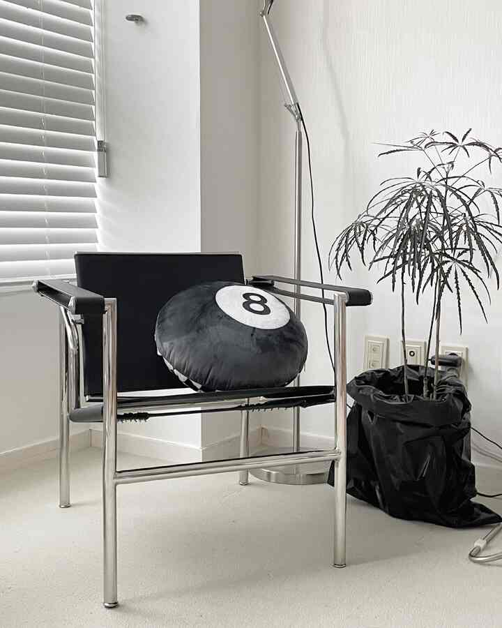 モダンなシルバーフレームのアームチェアと黒いクッション、フロアランプと植物が配置された自然な色調のシンプルなコーナースペース