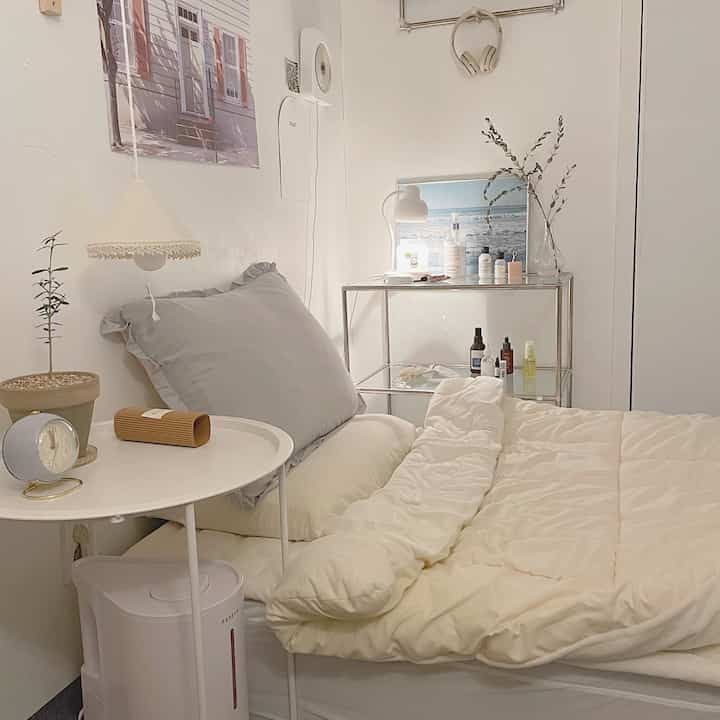 Small bedroom in white and gray tones featuring a cozy bed, side table, and glass shelving with storage ideas in a natural modern setting