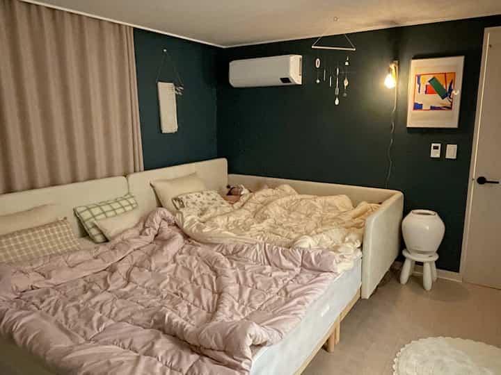 A warm bedroom with white and beige tones featuring a large family bed, wall lamp, and mobile decoration