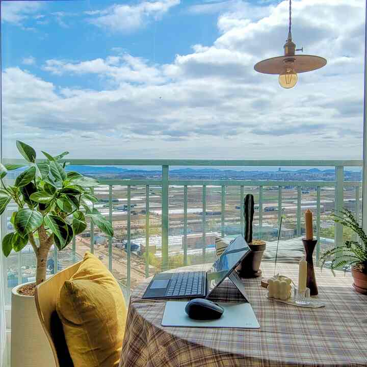 A bright balcony space with natural light and green plants featuring a round dining table with checkered tablecloth for a cozy remote work setting