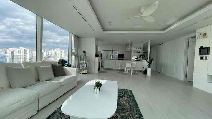 Bright white-toned living room connected to kitchen with large floor-to-ceiling windows and modern furniture, creating a clean open space