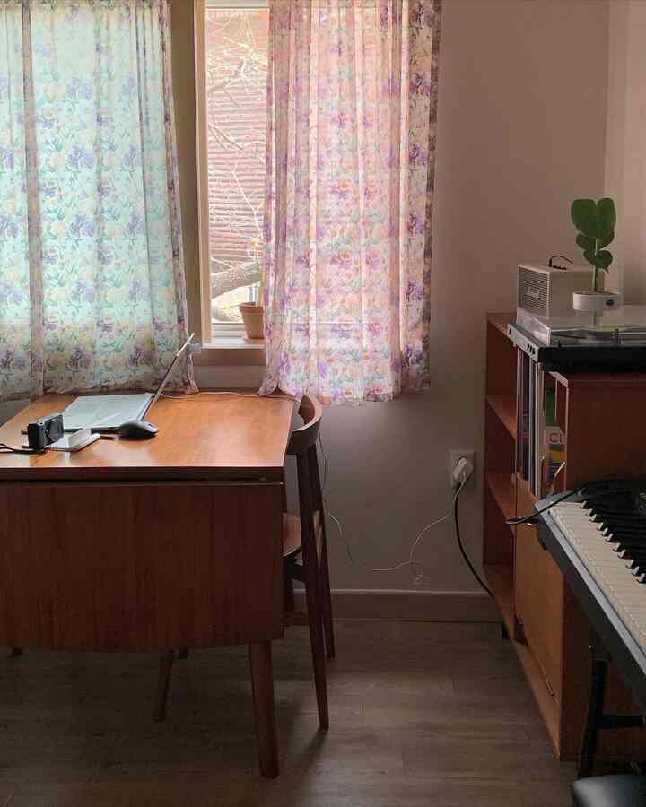 Cozy small home office with wood tone furniture and floral curtains, bathed in soft natural light