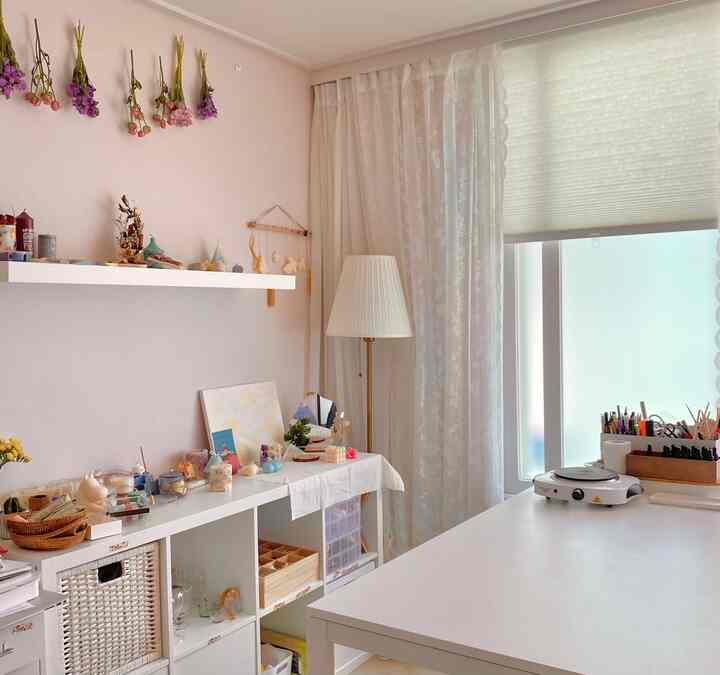White and natural toned home workshop featuring a large desk, sheer curtains, and neatly arranged candles in a cozy workspace