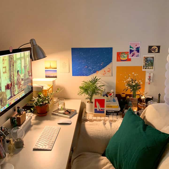Cozy single-person home office and reading space with warm lighting, green plants, posters decorating the wall