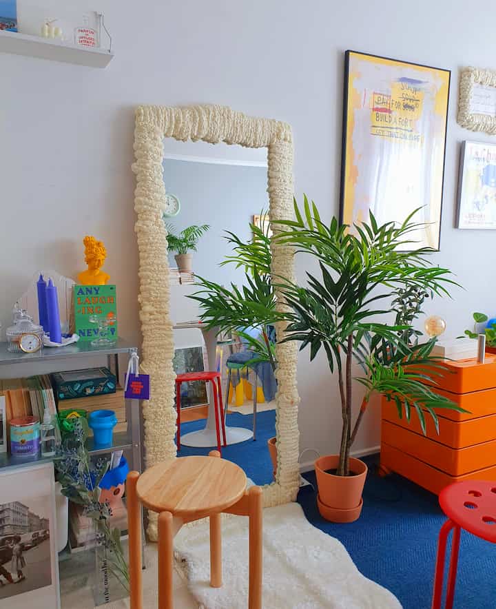 A natural cafe-style dining room with blue rug, wooden stool, and an orange dresser as a point of interest in a cozy atmosphere