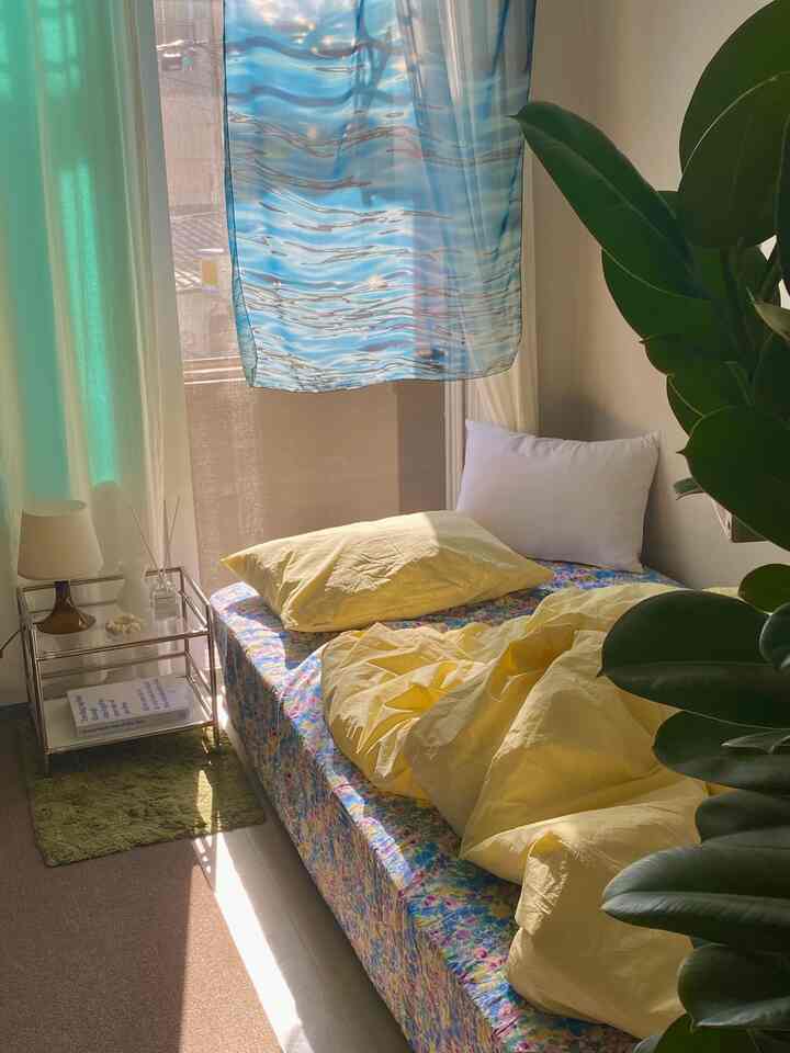 Studio bedroom featuring yellow bedding and blue fabric poster with natural plant, creating cozy and vibrant atmosphere