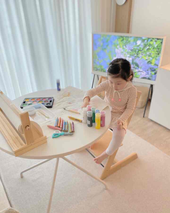 白い円形テーブルとトリップトラップチェアがあるナチュラルな子供部屋、絵を描く子供が配置された印象的な空間