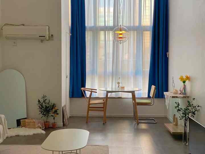 A simple and natural dining room with white walls and blue curtains, featuring a round dining table and natural wood chairs