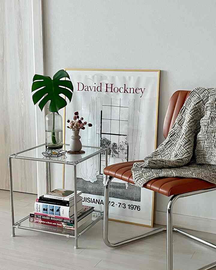 Beige-toned floor and wall with a clear glass side table, brown leather chair, and Monstera plant creating a simple, natural living room interior