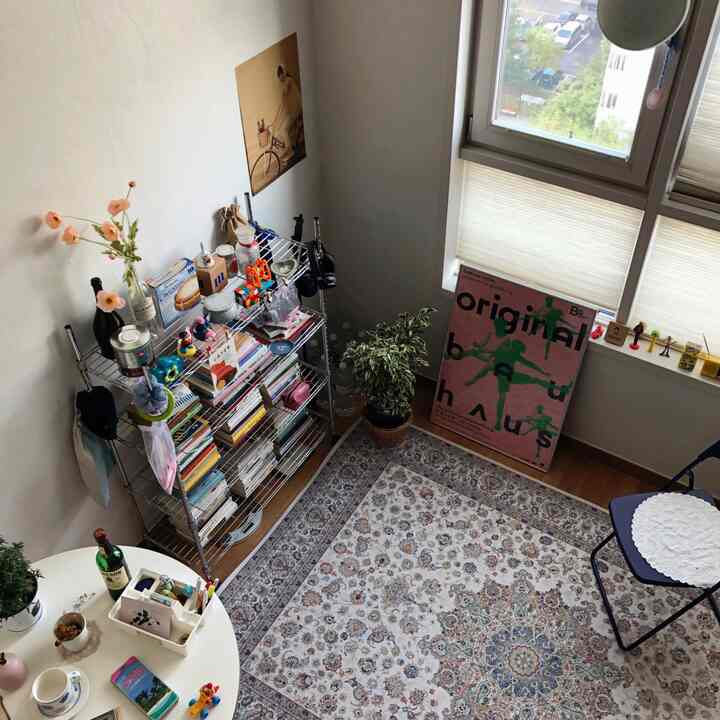 白を基調とした小さな部屋、ペルシャ絨毯のラグと本棚、丸テーブルが配置された雰囲気のあるカフェ風インテリア