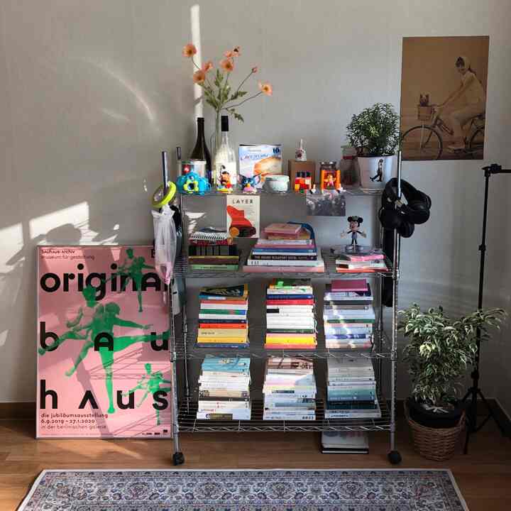 ネイビーとライトブラウンの色調のリビング、中央に金属製の本棚があり、本や装飾品が並び、壁にはポスターと植物が配置された自然な雰囲気のあるインテリア