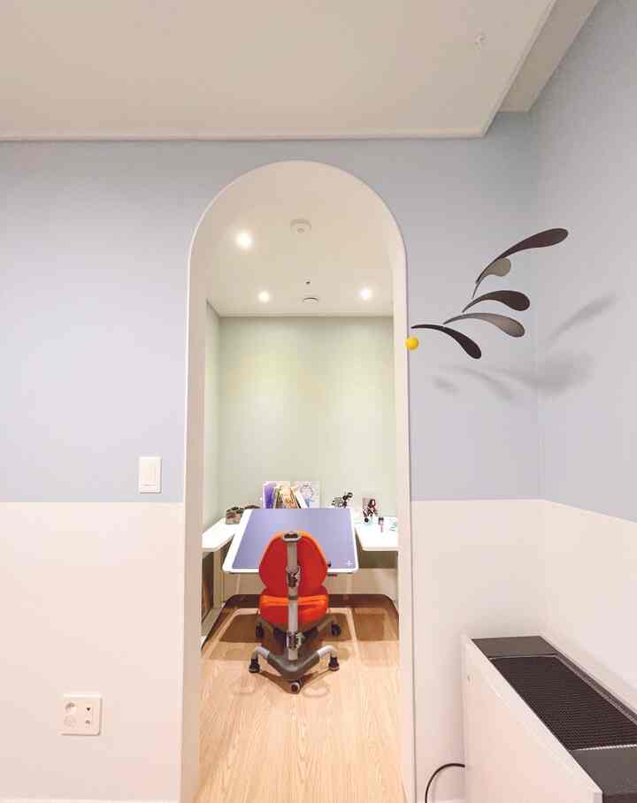 A kids' study room with mint and pastel blue two-tone walls, featuring an arched doorway, bright orange desk chair, and tidy desk setup