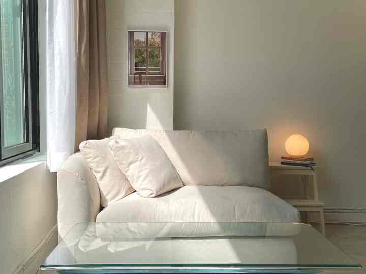 Natural-toned living room in white, featuring a white sofa, beige curtains and a round lamp on side table with a simple cozy atmosphere