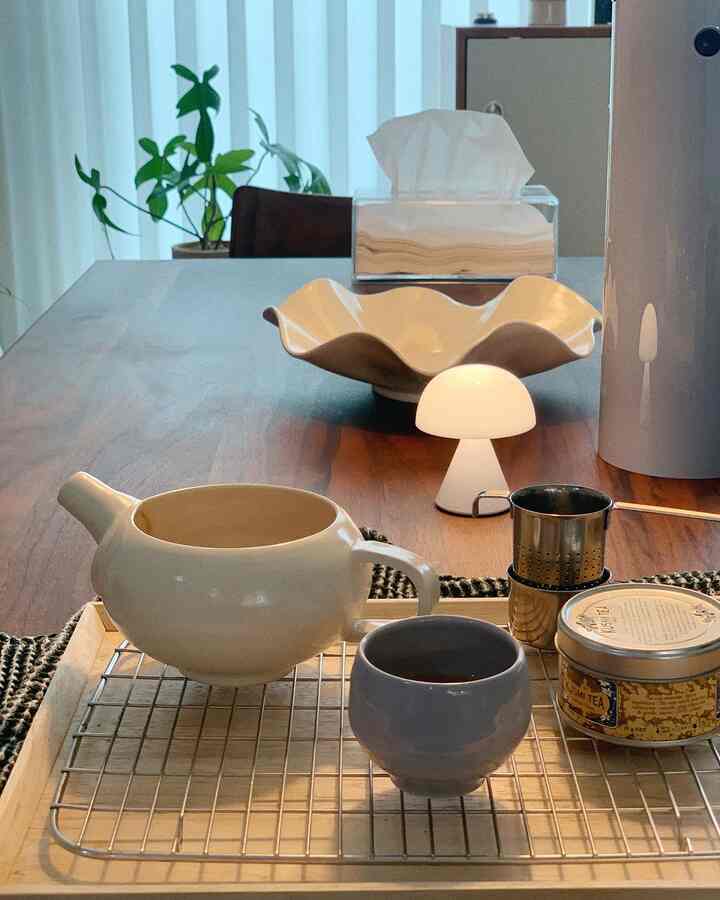 柔らかなホワイトと温かみのあるブラウンのダイニング、木製テーブルの上に陶器のティーカップとミニマッシュルームランプが配置された雰囲気のあるインテリア