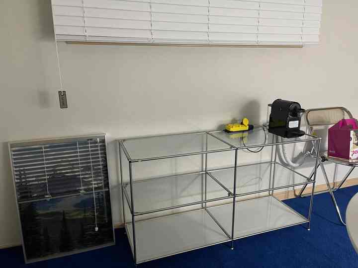 Kitchen space with white blinds and transparent modular shelving, featuring a black capsule coffee machine and folding chair in a clean modern interior