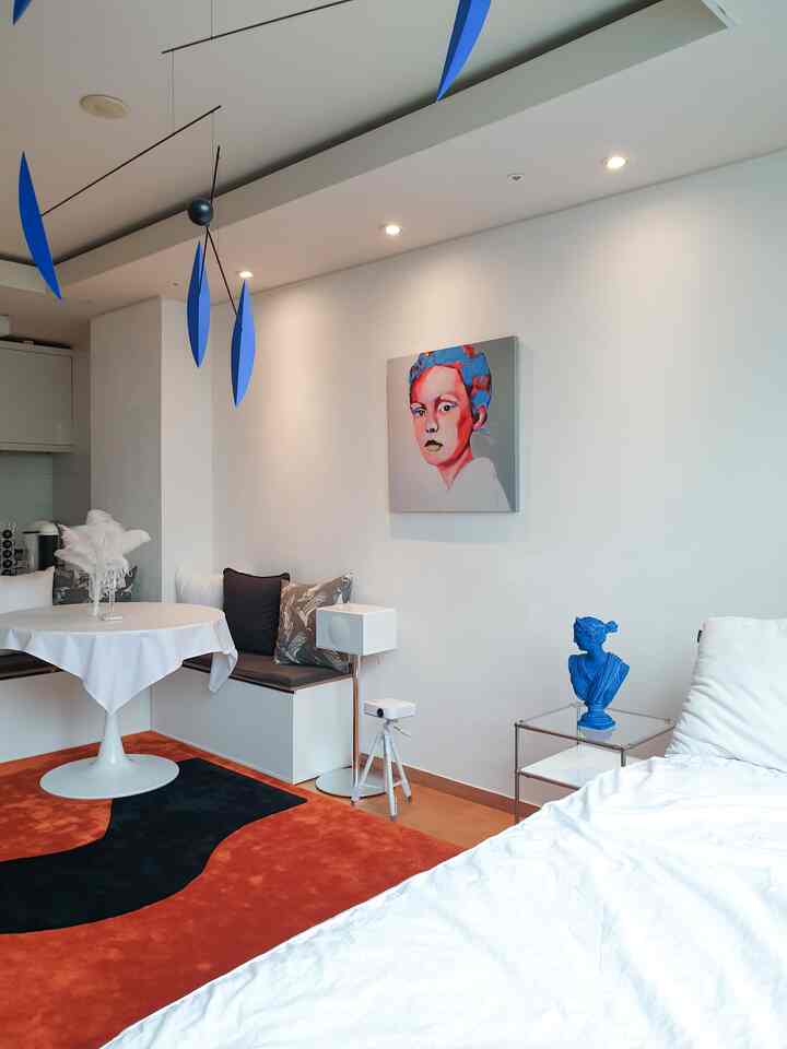 White and orange toned studio bedroom featuring modern dining table, blue mobile and sculpture in a stylish space
