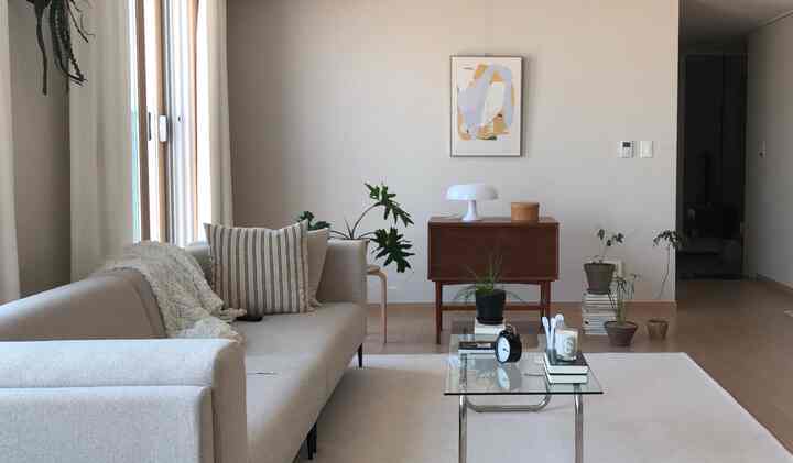 Bright toned living room featuring beige sofa, wooden console table, plants, and table lamp creating a natural atmosphere