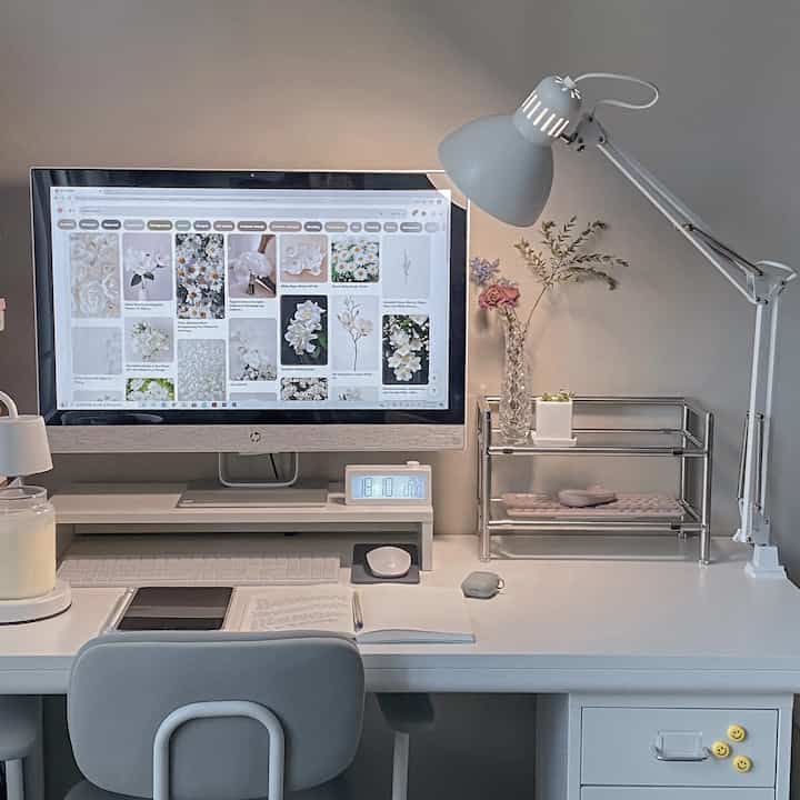 白を基調としたホームオフィス、白いデスクとモニター、照明、花瓶が配置された清潔感のある作業空間