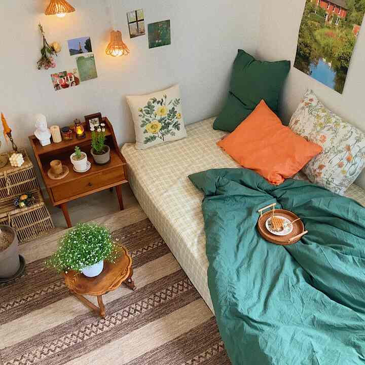 ナチュラルトーンのワンルーム寝室、ヴィンテージのサイドテーブルと植物が配置された居心地の良い空間