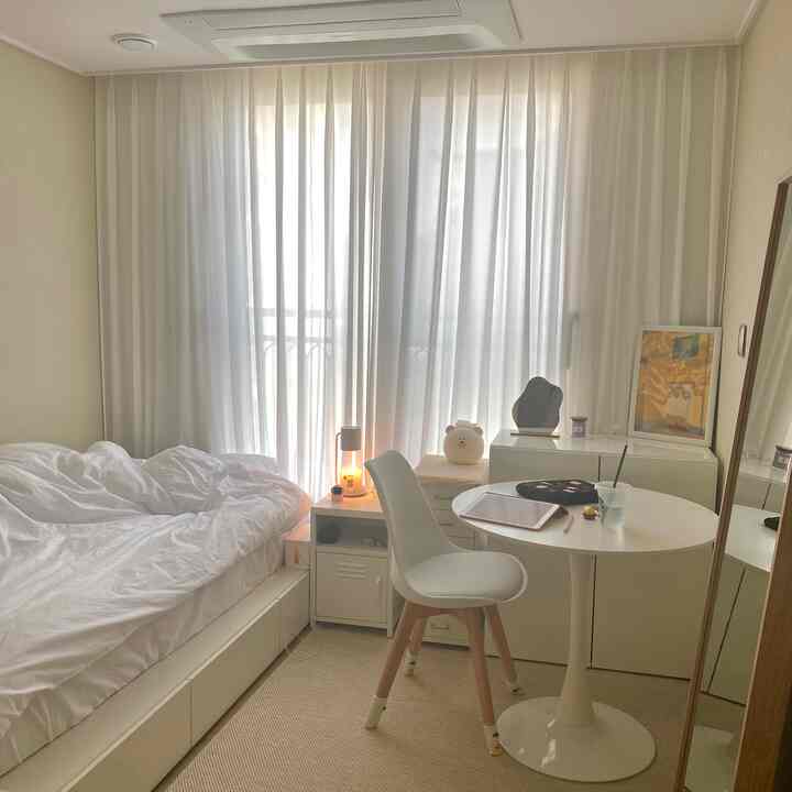 Soft white-toned small bedroom featuring white bed, nightstand, round table, and chair in a simple modern space