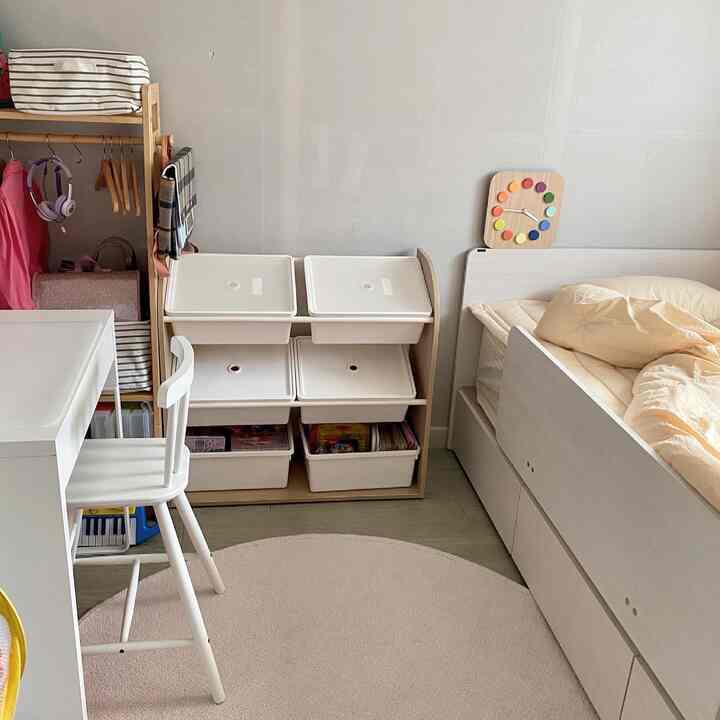 A cozy kids' room in white and natural tones, featuring a desk, bed, and organized toy storage