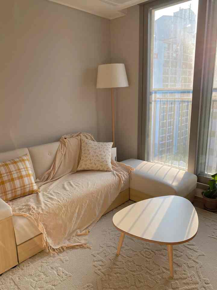 Beige and white toned living room featuring wood-tone sofa, coffee table, and floor lamp with warm and cozy atmosphere