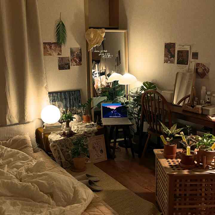 Natural-toned small bedroom featuring wooden chair, many plants, lamps, and mirrors creating cozy atmosphere