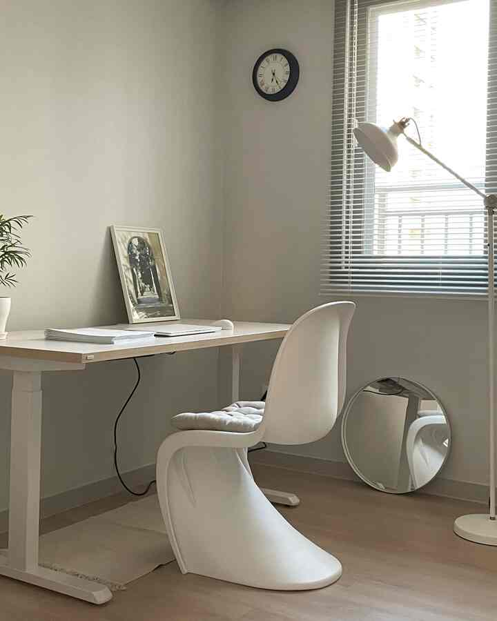 A simple study room with white and natural tones featuring a desk, chair, and blinds neatly arranged