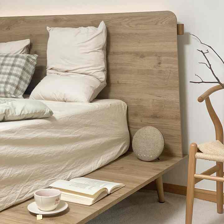 A natural wood tone and beige bedroom featuring a wooden bed, pillows, an open book, and a teacup creating a simple and cozy atmosphere