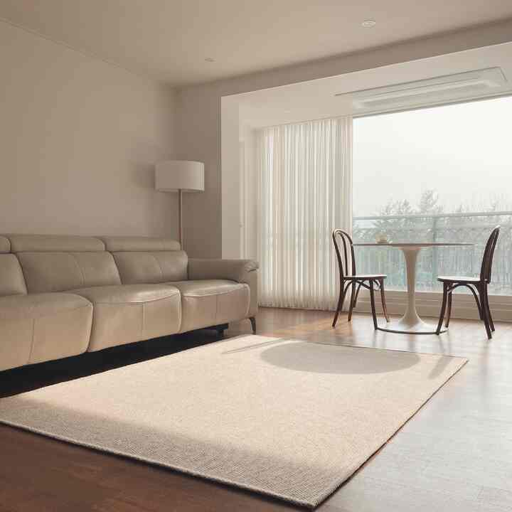 Beige-toned living room featuring a comfortable leather sofa, large rug, and round dining table bathed in natural light with minimal decor